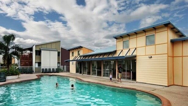 Une piscine entourée de bâtiments dotés de grandes fenêtres, sous un ciel dégagé.
