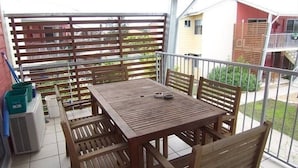 Une table et des chaises en bois sur un balcon, avec vue sur des immeubles et de la verdure.