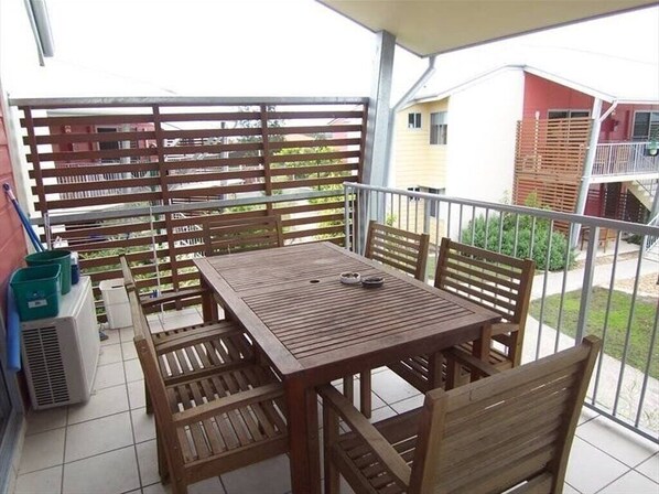 A wooden table and chairs on a balcony with a view of buildings and greenery.