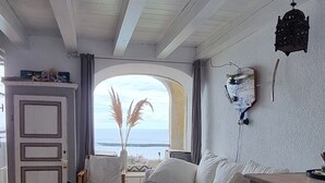 A room with a bed, a chair, a small table, a decorative wall piece, and a view of the sea. - Holiday Home 'Il Carrubo' with Sea View, Wi-Fi and Air Conditioning (Finale Ligure)