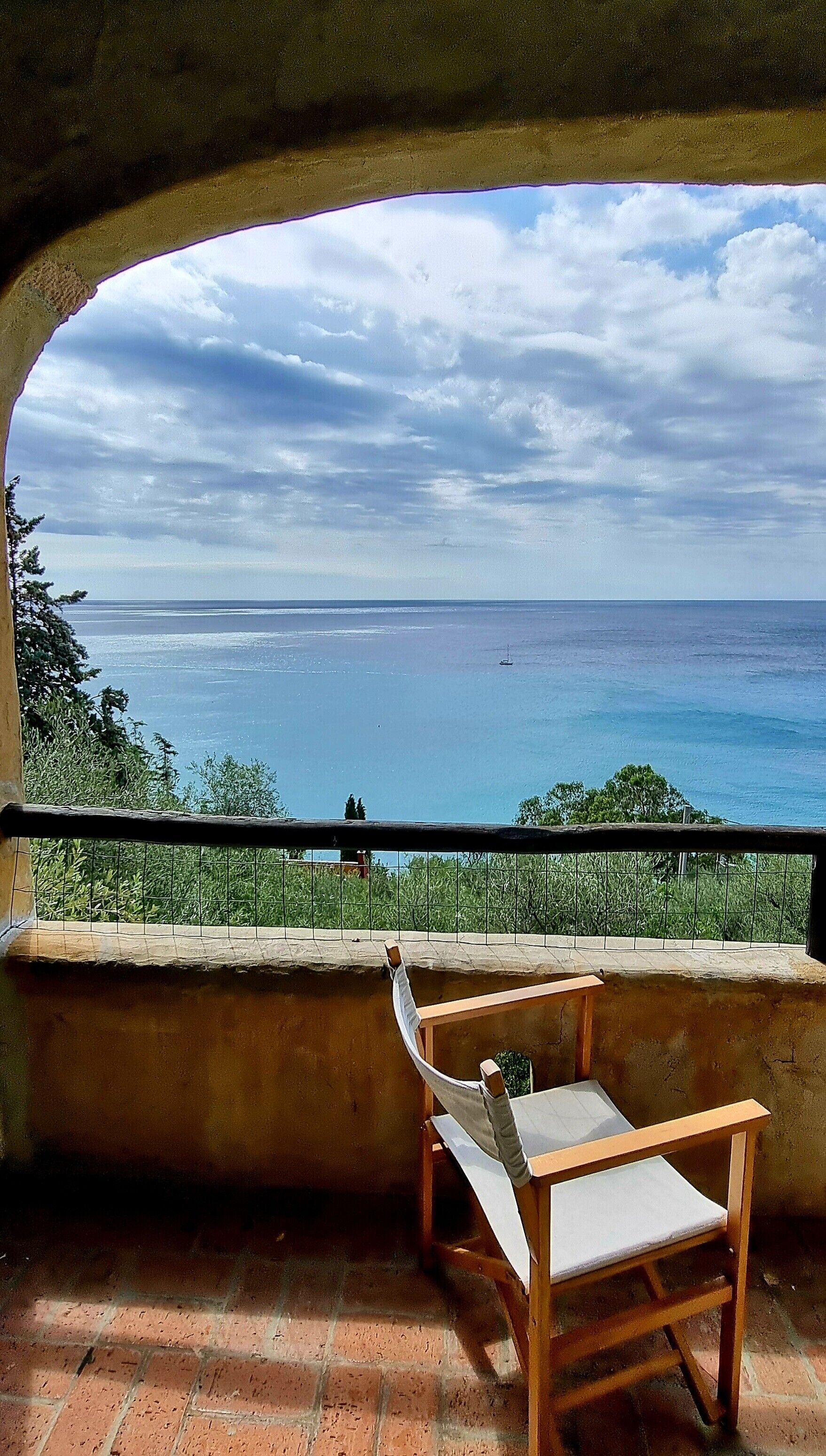 A wooden chair with a cushion on a balcony overlooking a body of water.