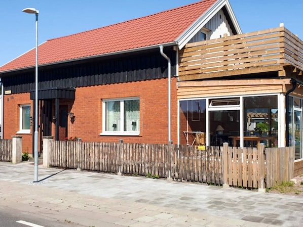 A two-story building with a red-tiled roof, a wooden fence, and a paved sidewalk. - 4 Star Holiday Home in Kattarp (Kattarp)