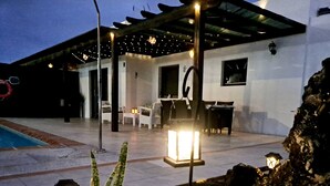 Eine überdachte Terrasse im Freien mit Sitzgelegenheiten, einem Pool und einem gut beleuchteten Garten.