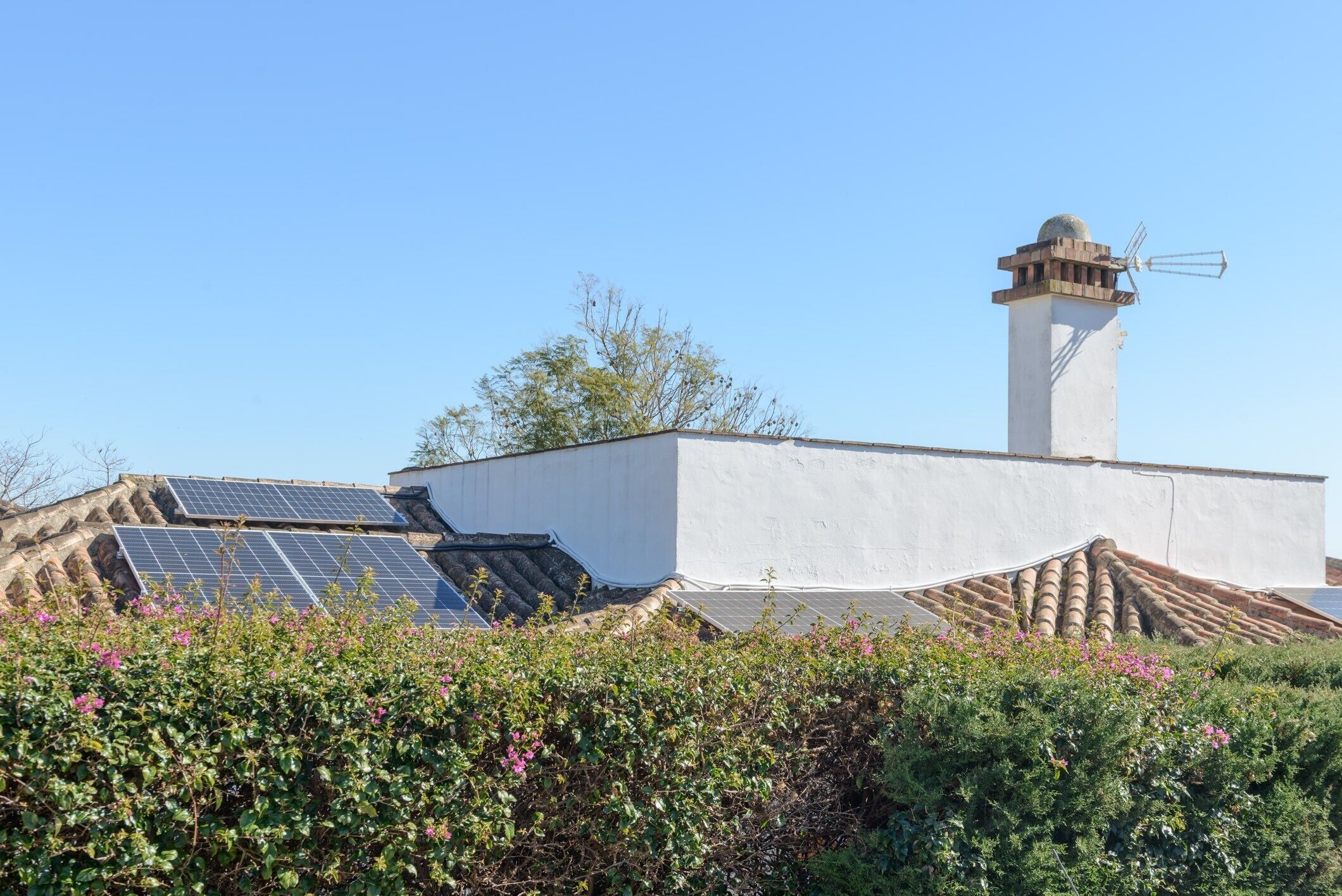 Ein Gebäude mit weißer Fassade, einem Schornstein und Solaranlage auf dem Dach.