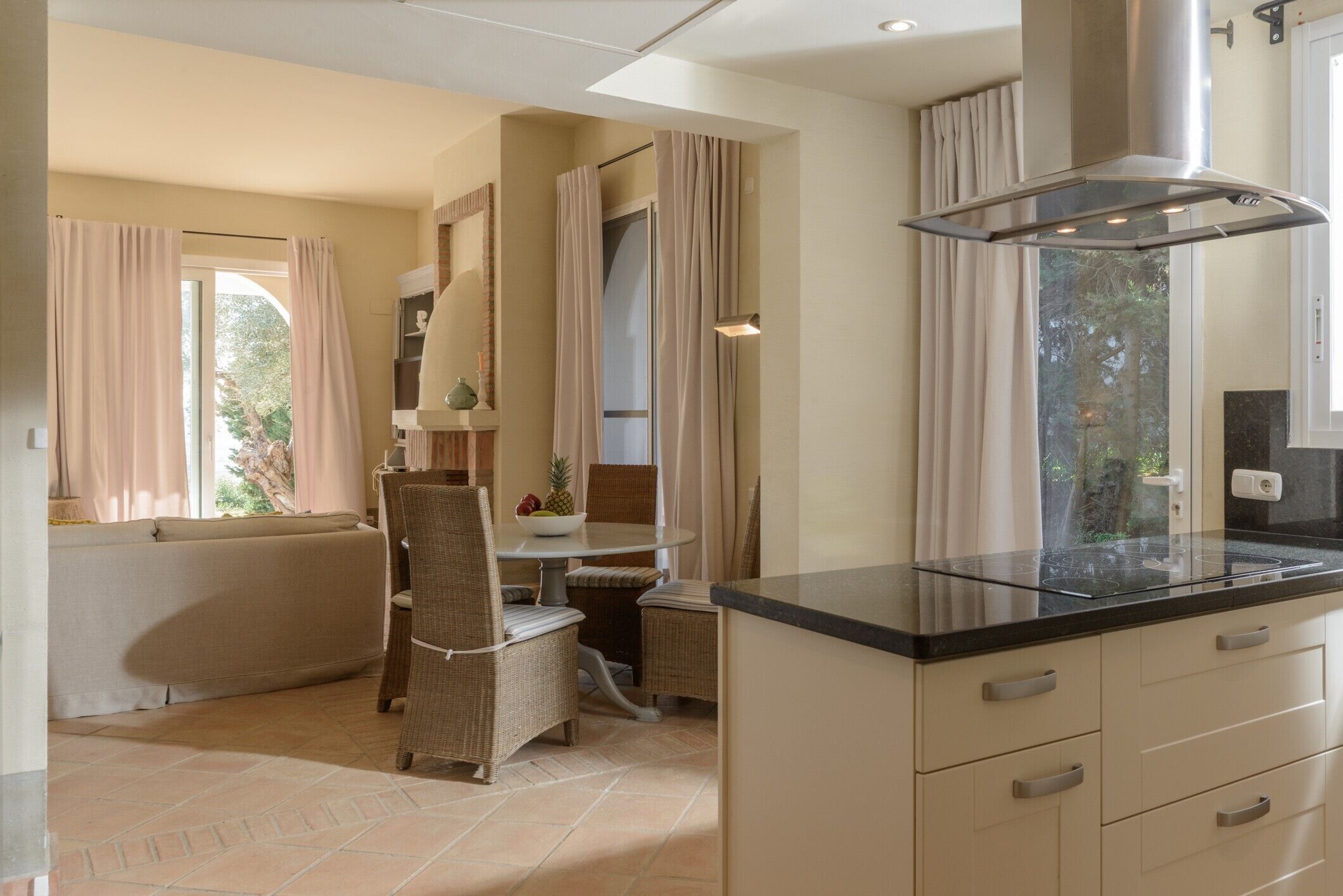A kitchen with a modern stove, a dining area with wicker chairs, and a view of the outdoors through the window.