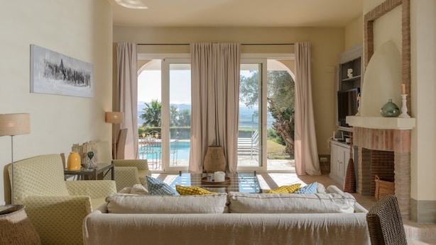 A living room with a sofa, a TV, and a fireplace. There is a large window with curtains and a view of a pool and greenery. - Villa 'Lirio' with Mountain Views, Wi-Fi, and Air Conditioning (Benalup-Casas Viejas)