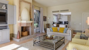 A living room with a fireplace, sofa, coffee table, and a kitchen area in the background. - Villa 'Lirio' with Mountain Views, Wi-Fi, and Air Conditioning (Benalup-Casas Viejas)