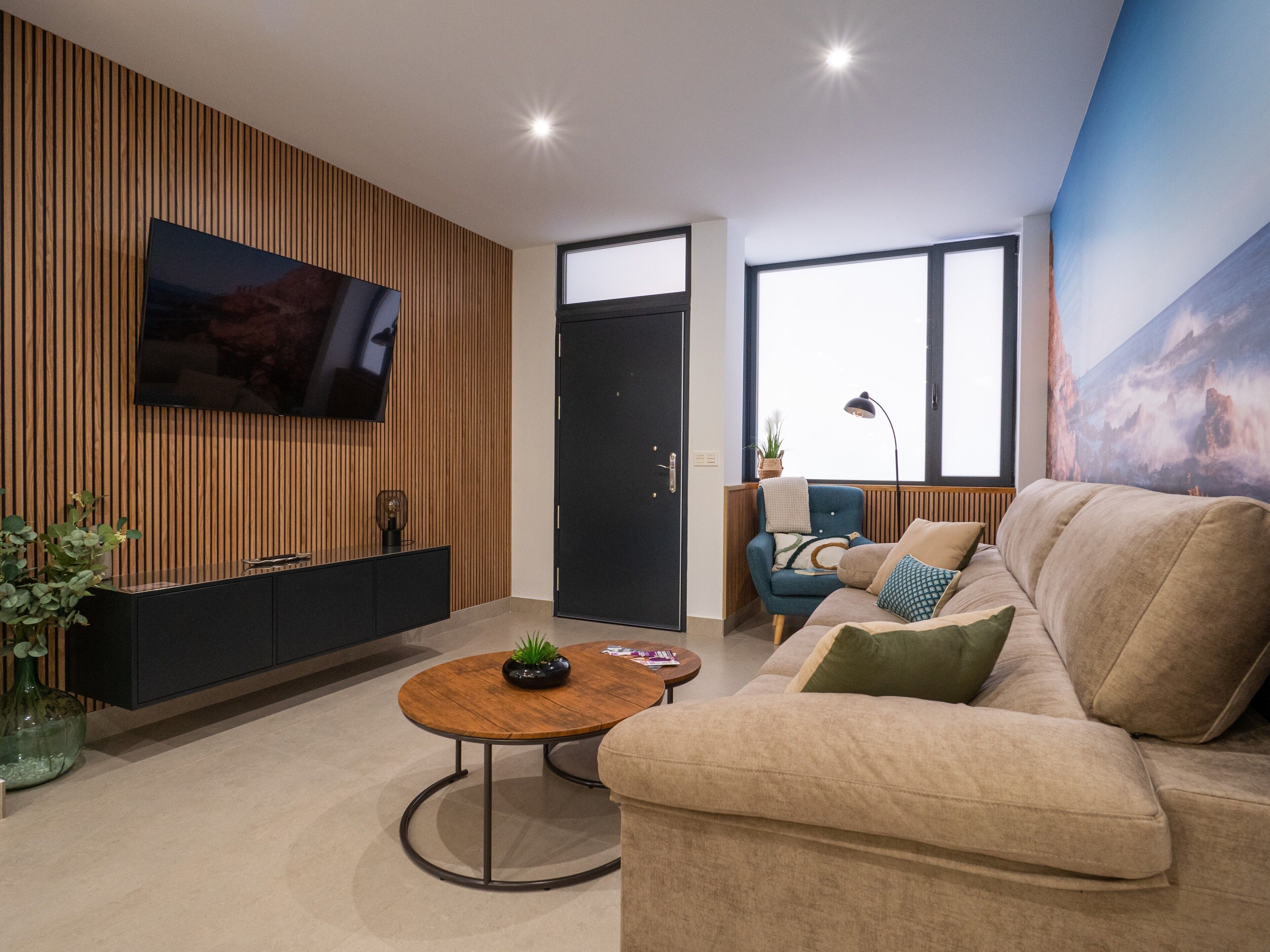 Ein modernes Wohnzimmer mit Fernseher, Sofa, Couchtisch und einem großen Fenster.