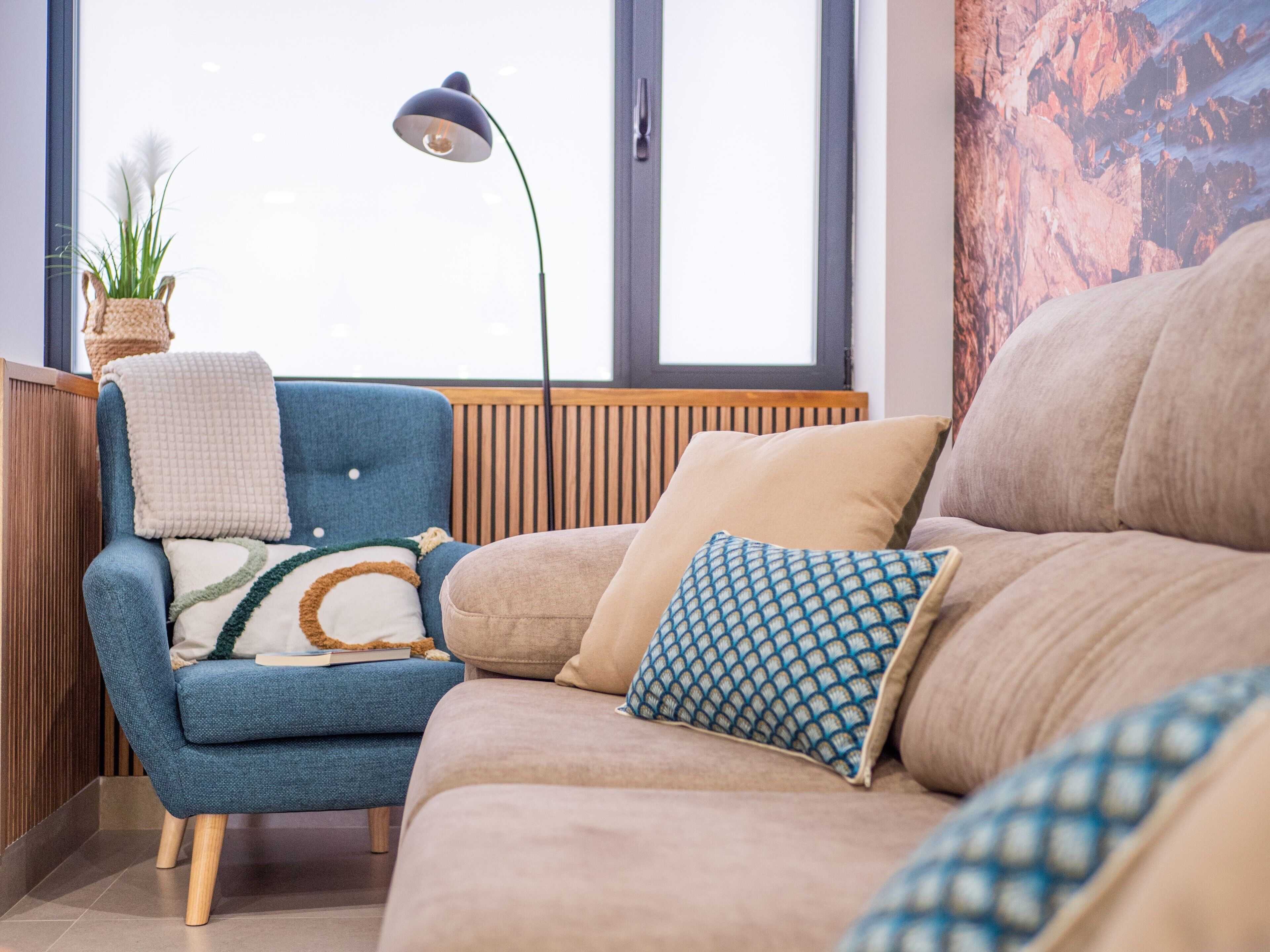 Ein modernes Wohnzimmer mit einem blauen Sessel, einem beigen Sofa und Kissen mit Muster.