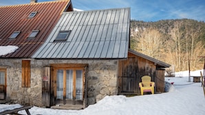 Un edificio rústico de piedra con puerta y ventanas de madera, techo de metal y suelo cubierto de nieve.
