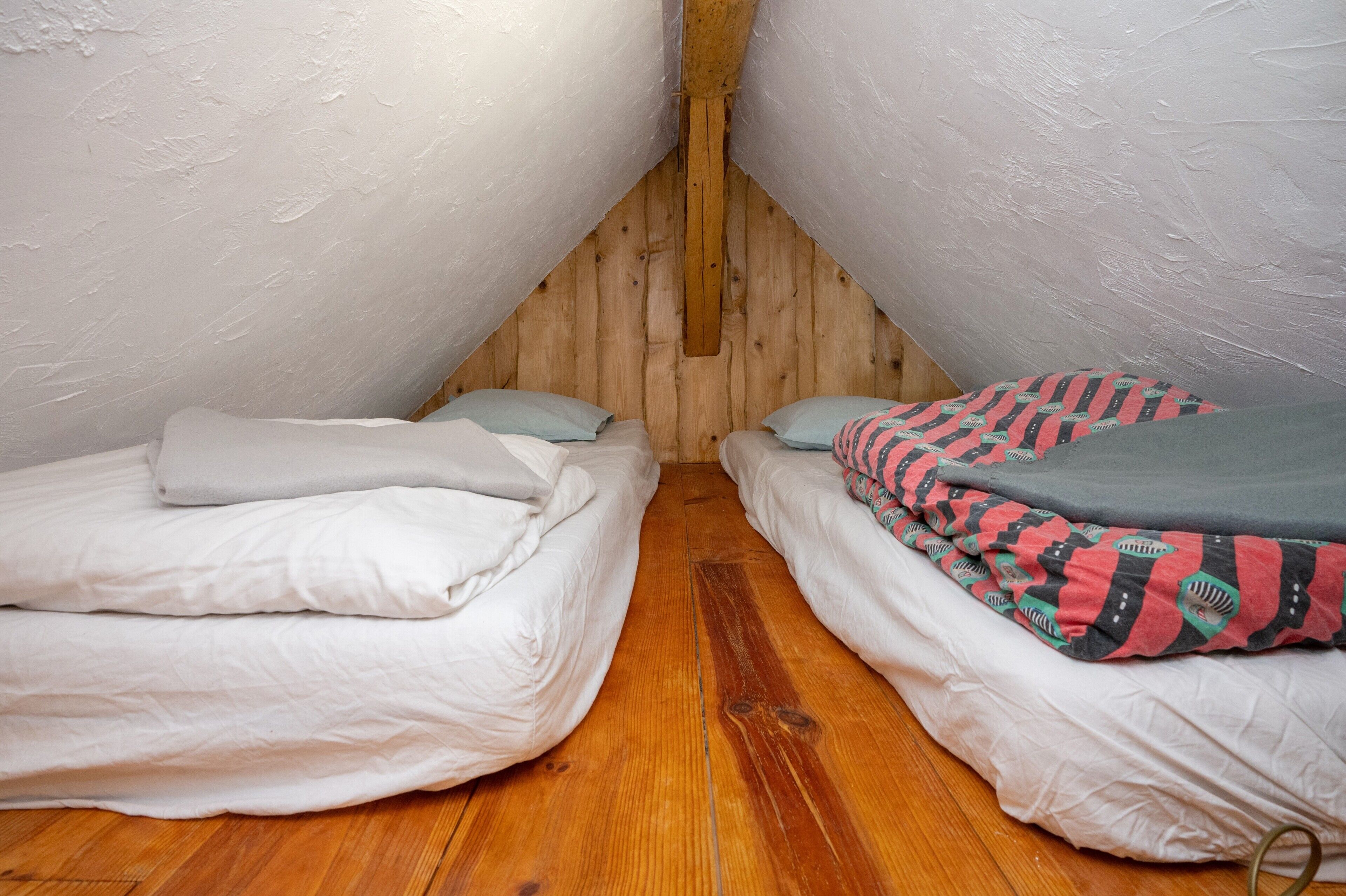 A small attic bedroom with two beds, wooden walls, and a sloped ceiling.