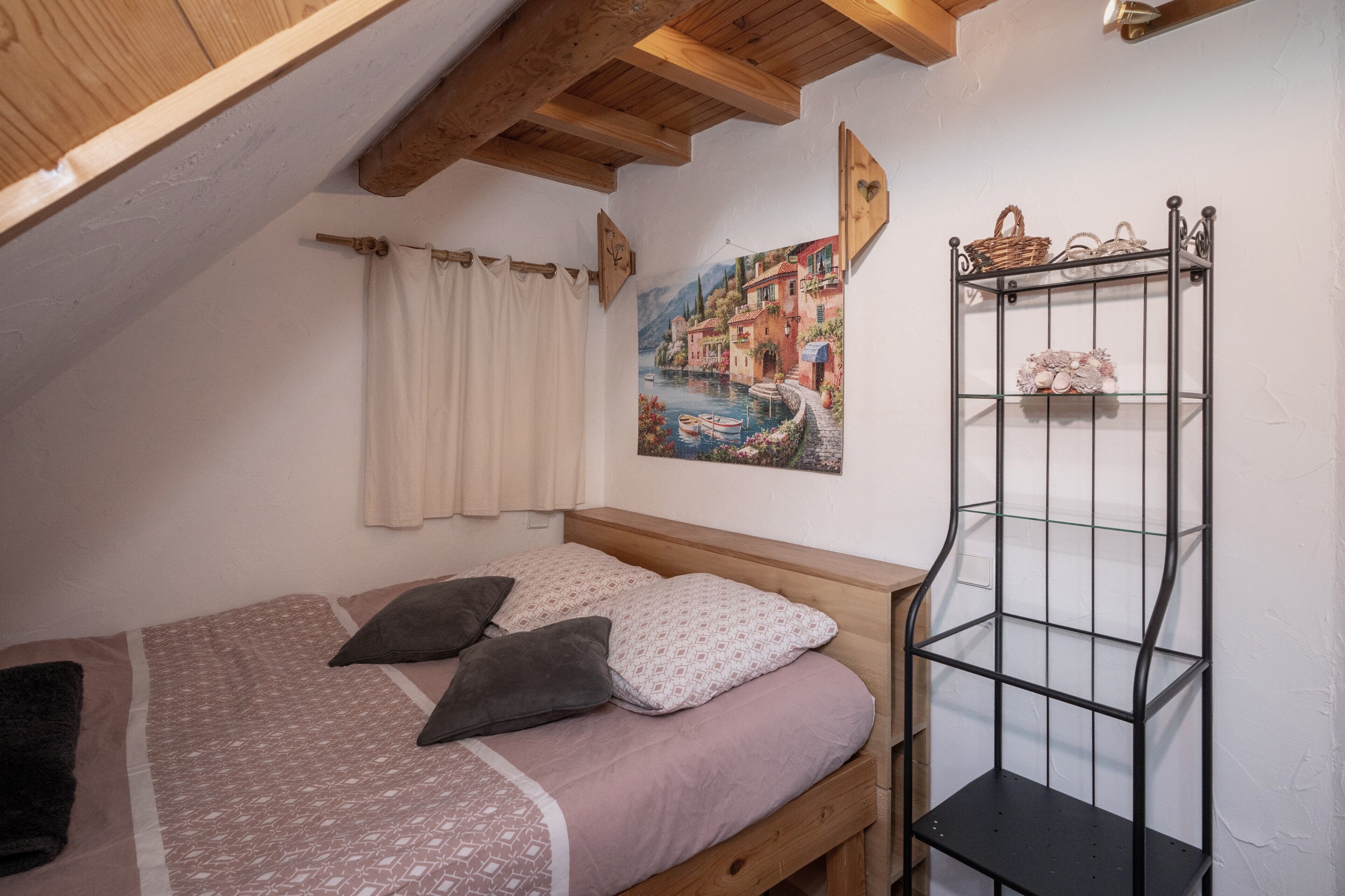 Ein Schlafzimmer mit Bett, Ablagefläche, Gemälde und einem Fenster mit Vorhängen.