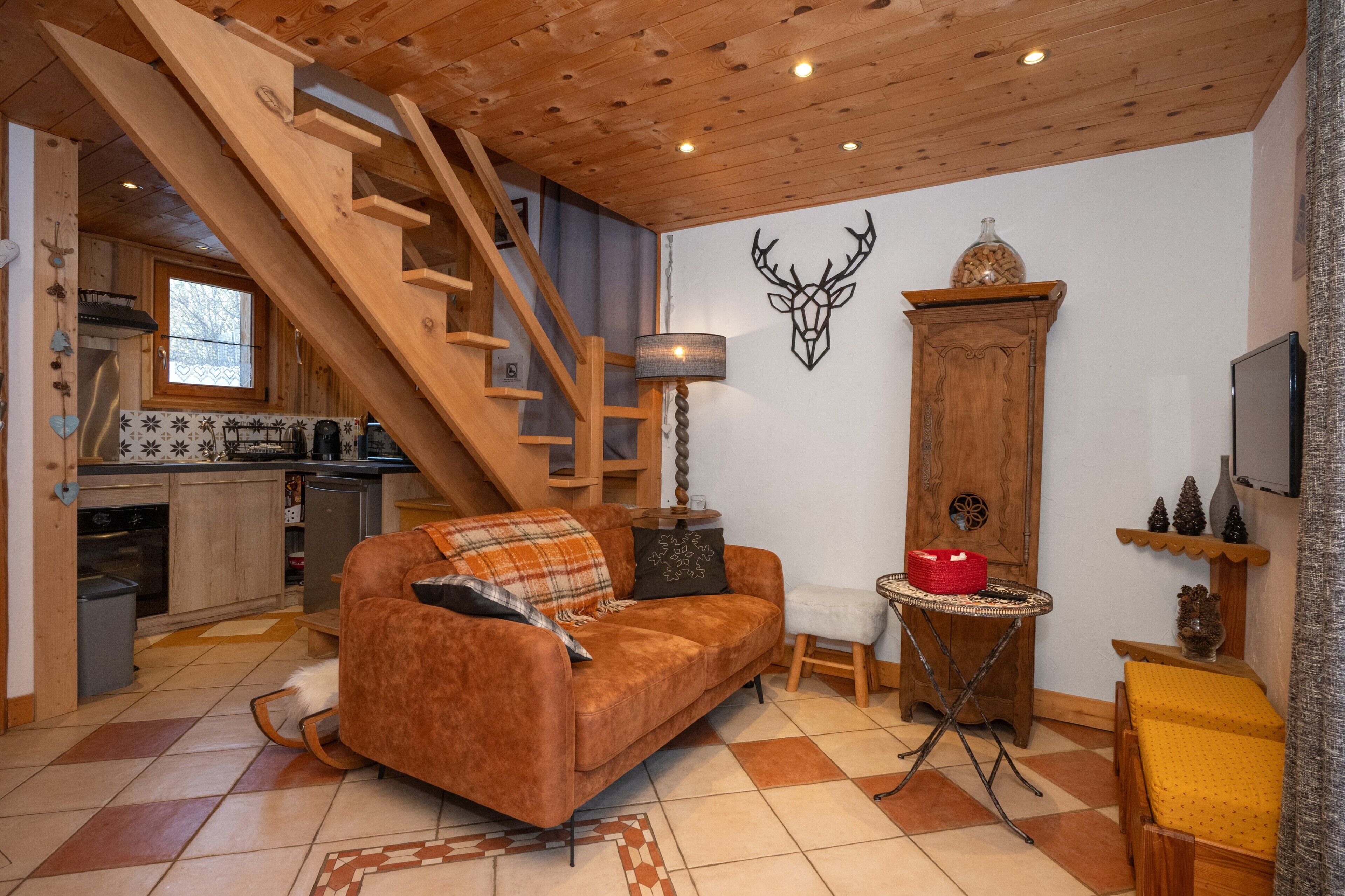 A cozy living area with a wooden staircase, a sofa, a small table, and a kitchen in the background.