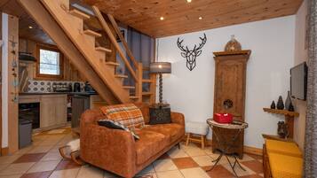 A cozy living area with a wooden staircase, a sofa, a small table, and a kitchen in the background.