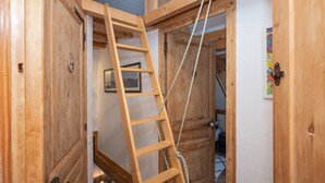 Una escalera de madera apoyada en una puerta en una habitación con paredes y techo de madera con vigas a la vista.