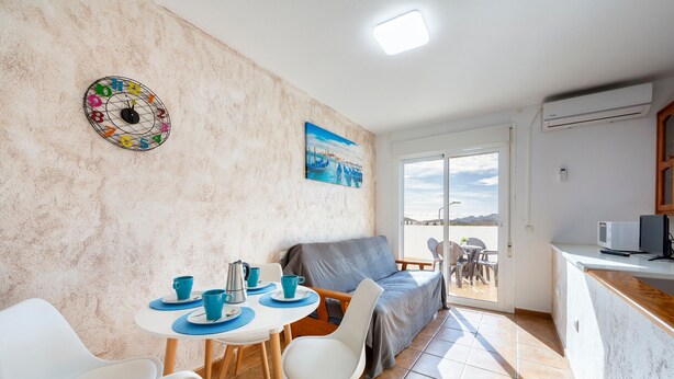 A room with a dining table, chairs, a sofa, a painting, and a view through a door.