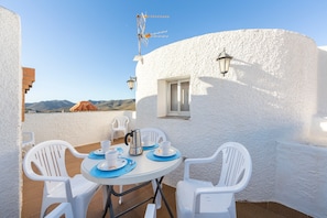 Eine Terrasse mit weißen Wänden, an einem Tisch für zwei Personen, zwei Stühlen, einem Fenster und einer Wandantenne.