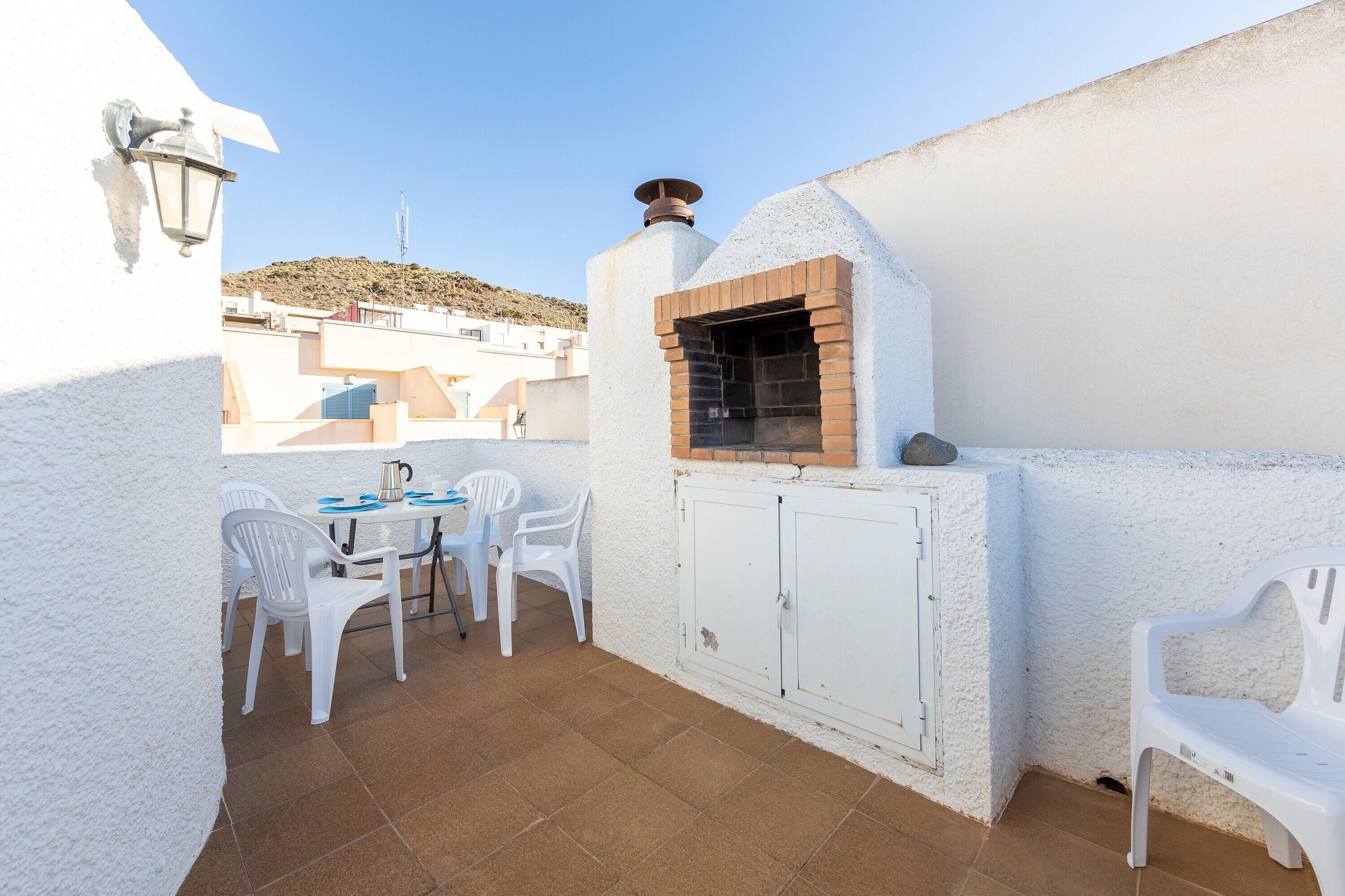 A patio with a brick oven, white chairs, and a table.