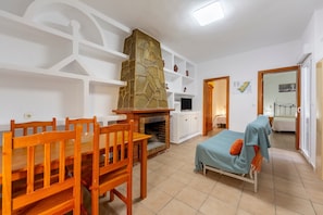 Ein Zimmer mit Esstisch, Stühlen, einem Steinkamin, einem Bett und einem Fernseher.