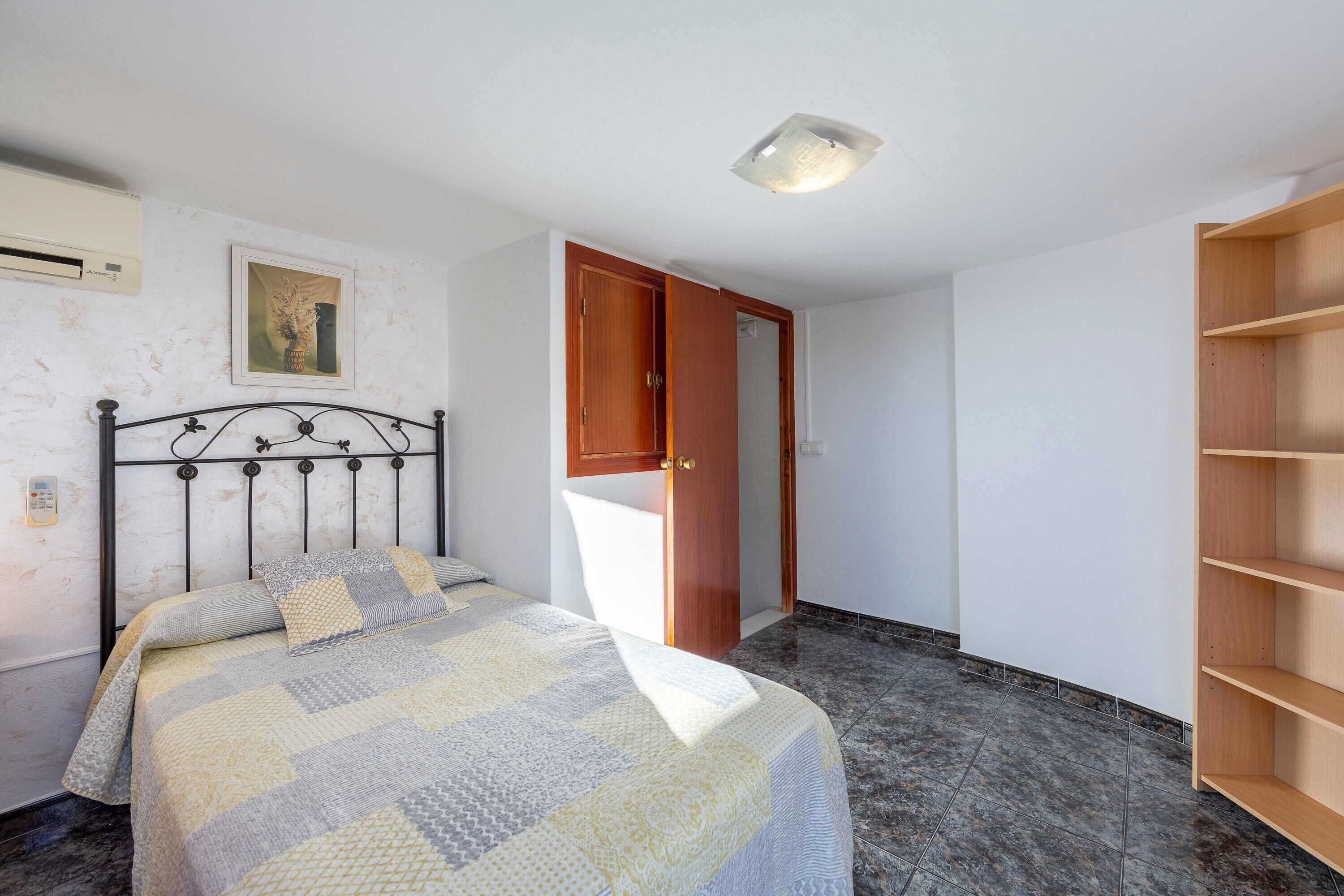 Un dormitorio con cama, armario, estantería e iluminación en el techo.