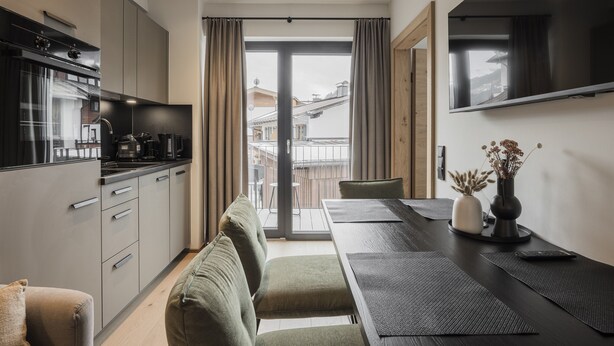 Une cuisine moderne dotée d’un four et d’une cuisinière encastrés, un coin repas avec une table et des chaises, et une vue sur la ville grâce à de grandes fenêtres.