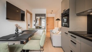 Une cuisine moderne dotée d’un four encastré, un coin repas avec une table et des chaises, et un espace de vie avec un canapé et un téléviseur.