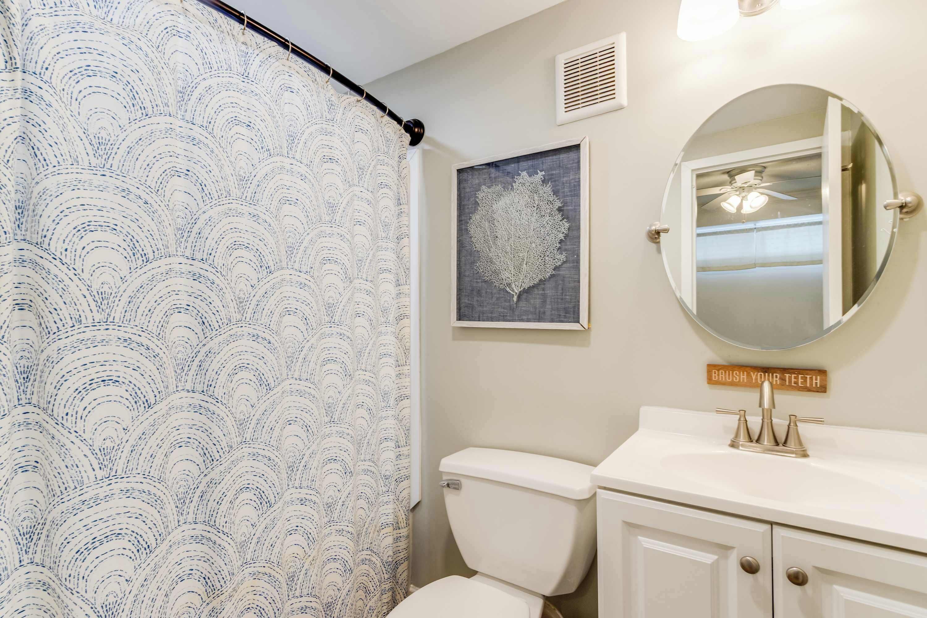 A bathroom with a toilet, a sink, a mirror, a shower curtain, and a wall-mounted sign.