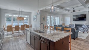 A spacious kitchen with a large island, dining area with wicker chairs, and a living room with a fireplace and sofas. - Private Pool Rehoboth Beach House Seven Bedrooms! (Dewey Beach)