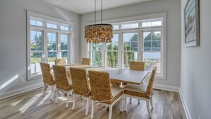 A dining room with a large table and wicker chairs, large windows, and a hanging light fixture. - Private Pool Rehoboth Beach House Seven Bedrooms! (Dewey Beach)