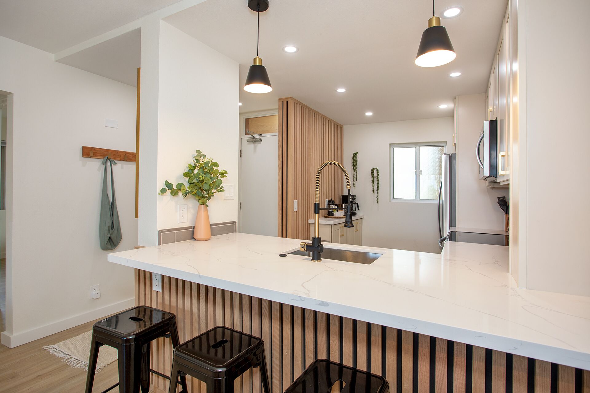 Une cuisine moderne dotée d’un îlot central, de luminaires suspendus et d’un mur d’accent en bois.