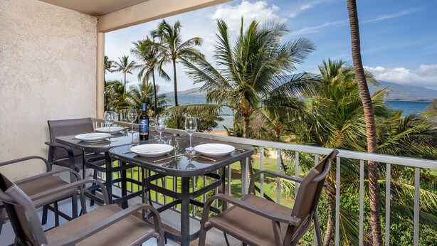 Ein Balkon mit Tisch für Zwei, Blick auf einen Strand mit Palmen und den Ozean.