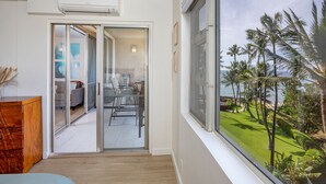 Ein Zimmer mit einer Schiebetür, die auf einen Balkon mit Blick auf Palmen und einen Strand führt.