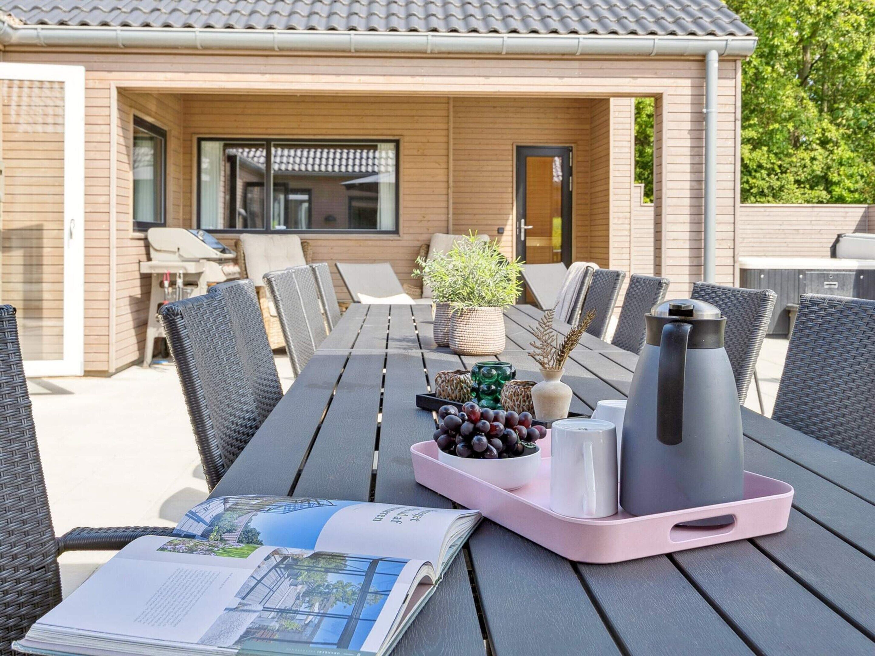 A wooden deck with a table set for dining, outdoor chairs, and a grill area in the background.