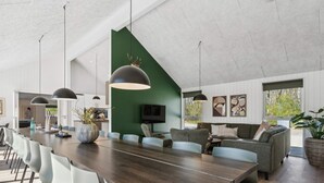Un'area pranzo moderna con un lungo tavolo in legno, sedie bianche e lampade a sospensione.
