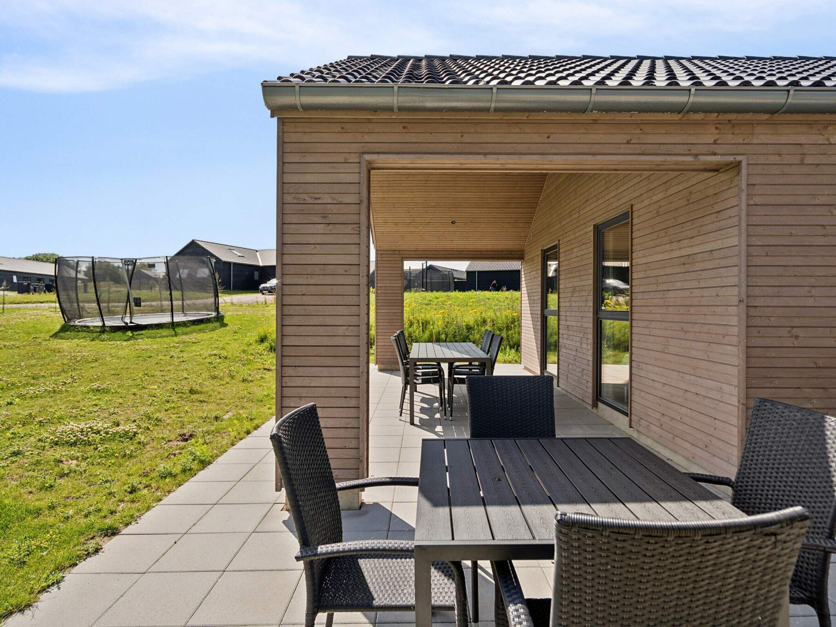 An outdoor patio with a table and chairs, a covered seating area, and a trampoline.