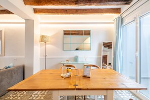 Un coin repas avec une table en bois, des chaises, une lampe, un miroir et une vue à travers une porte vitrée.
