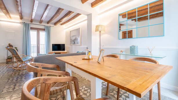 A spacious living area with a wooden dining table, chairs, a sofa, and a TV.