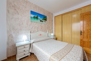 A bedroom with a bed, bedside tables, a nightstand, a wooden wardrobe, and a painting on the wall. - Apartment 'Maracas 1' with Shared Terrace and Air Conditioning (El Pozo de los Frailes)
