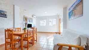 A dining area with a wooden table and chairs, a TV, and a plant.