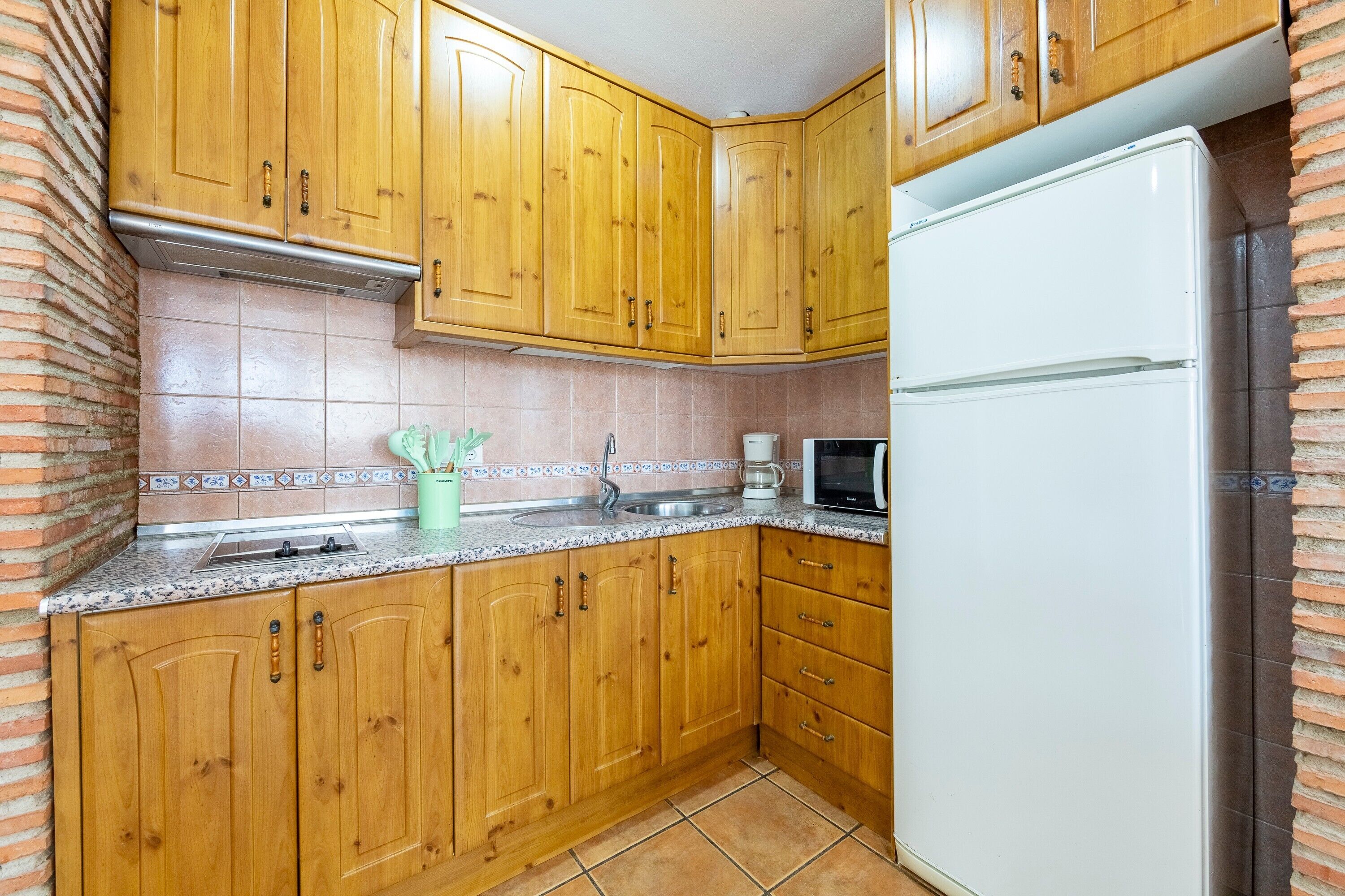 A kitchen with wooden cabinets, a white refrigerator, a microwave, and a sink.