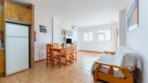 A kitchen with wooden cabinets, a white refrigerator, a dining table with chairs, and a sofa.