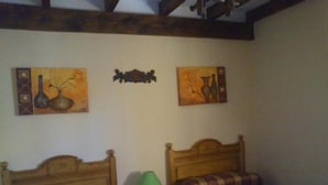 Quarto com duas camas de madeira, uma mesa de cabeceira com abajur e duas pinturas penduradas na parede.