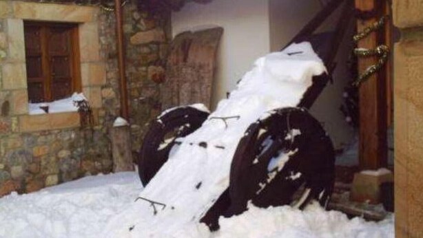Edifício de pedra com porta e janela de madeira, parcialmente coberto por neve.