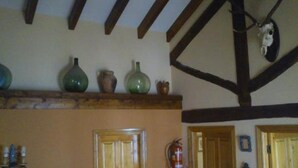 Quarto com vigas de madeira, lareira e uma estante com vasos decorativos.