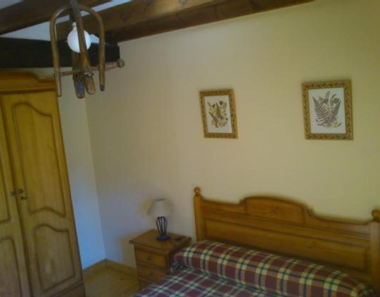 Un dormitorio con una cama de madera, una mesita de noche con una lámpara y dos cuadros enmarcados en la pared.