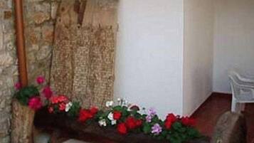 Un muro de piedra, un banco de madera con flores y una silla blanca en una esquina.