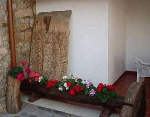 Un muro de piedra, un banco de madera con flores y una silla blanca en una esquina.