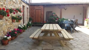 A stone patio with a wooden table and chairs, surrounded by potted plants and a wooden fence.