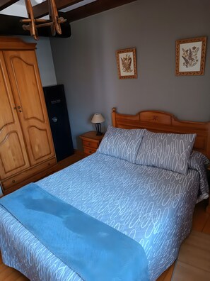 A bedroom with a bed, wooden wardrobe, nightstand, lamp, and two framed pictures on the wall.