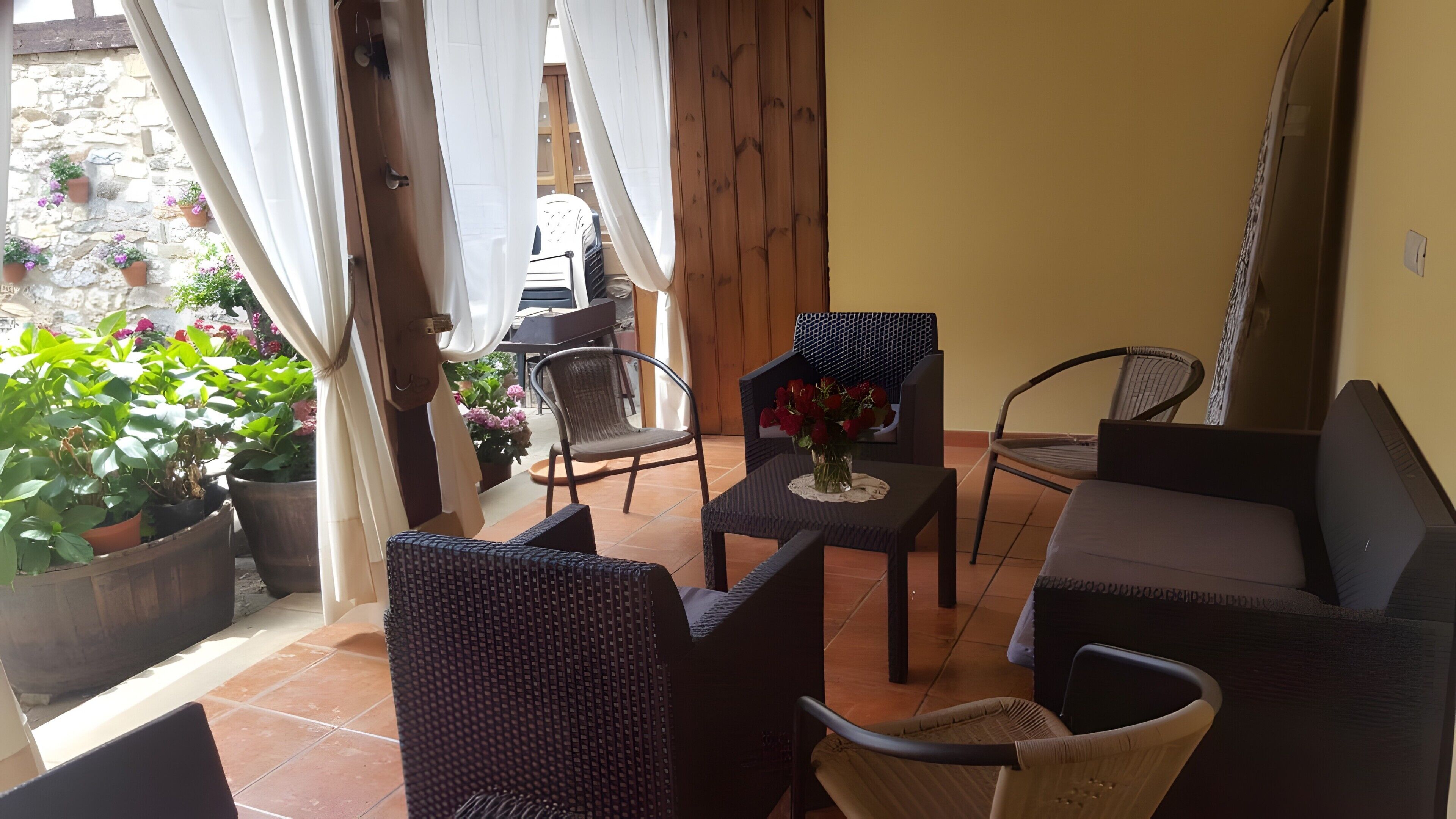 A patio area with wicker furniture, a table with a vase of flowers, and potted plants.